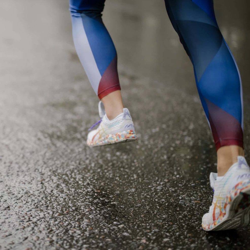 woman with tennis shoes and blue leggings running in the rain