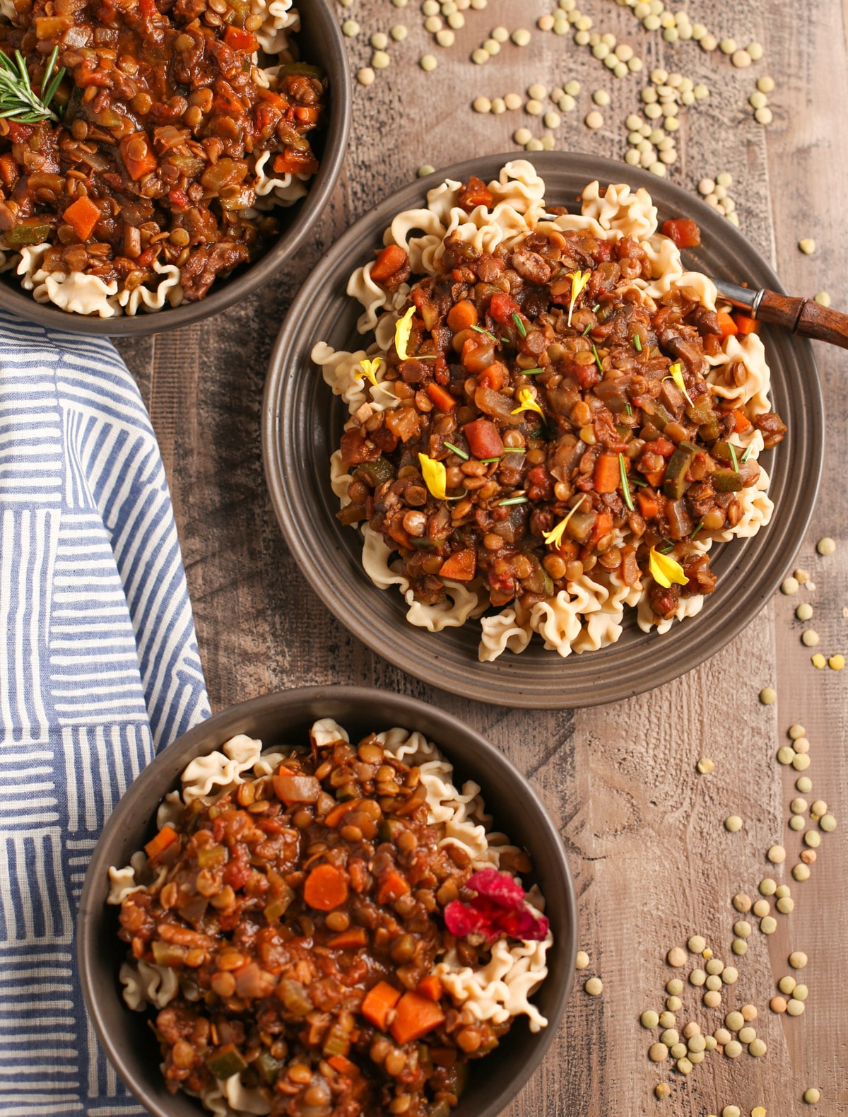 Three bowls of lentil bolognese with colorful garnishes